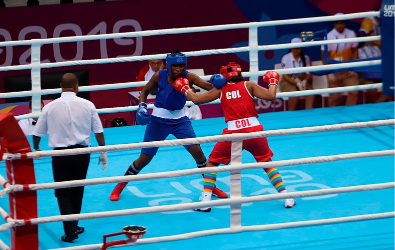 En la parte central de la imagen, aparecen dos boxeadores 
                            compitiendo, uno con uniforme rojo y el otro con uniforme azul. 
                            Al costado izquierdo de la lona, se encuentra el árbitro. 